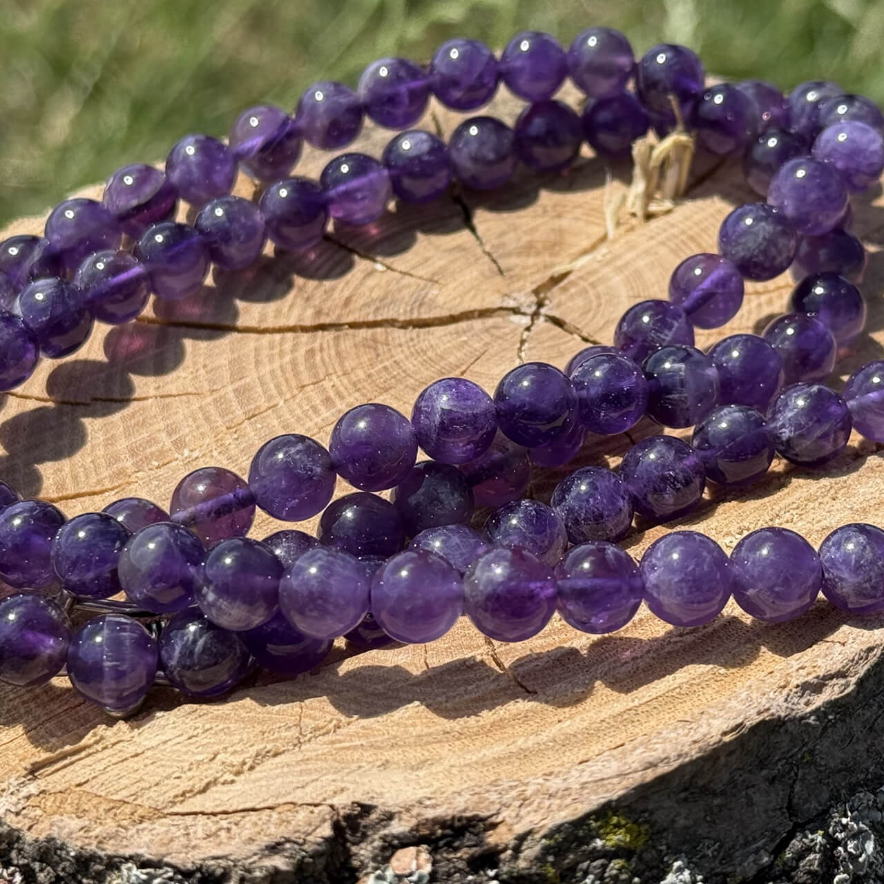 Amethyst crystal necklace displayed on wooden block with garden grass and greenery background