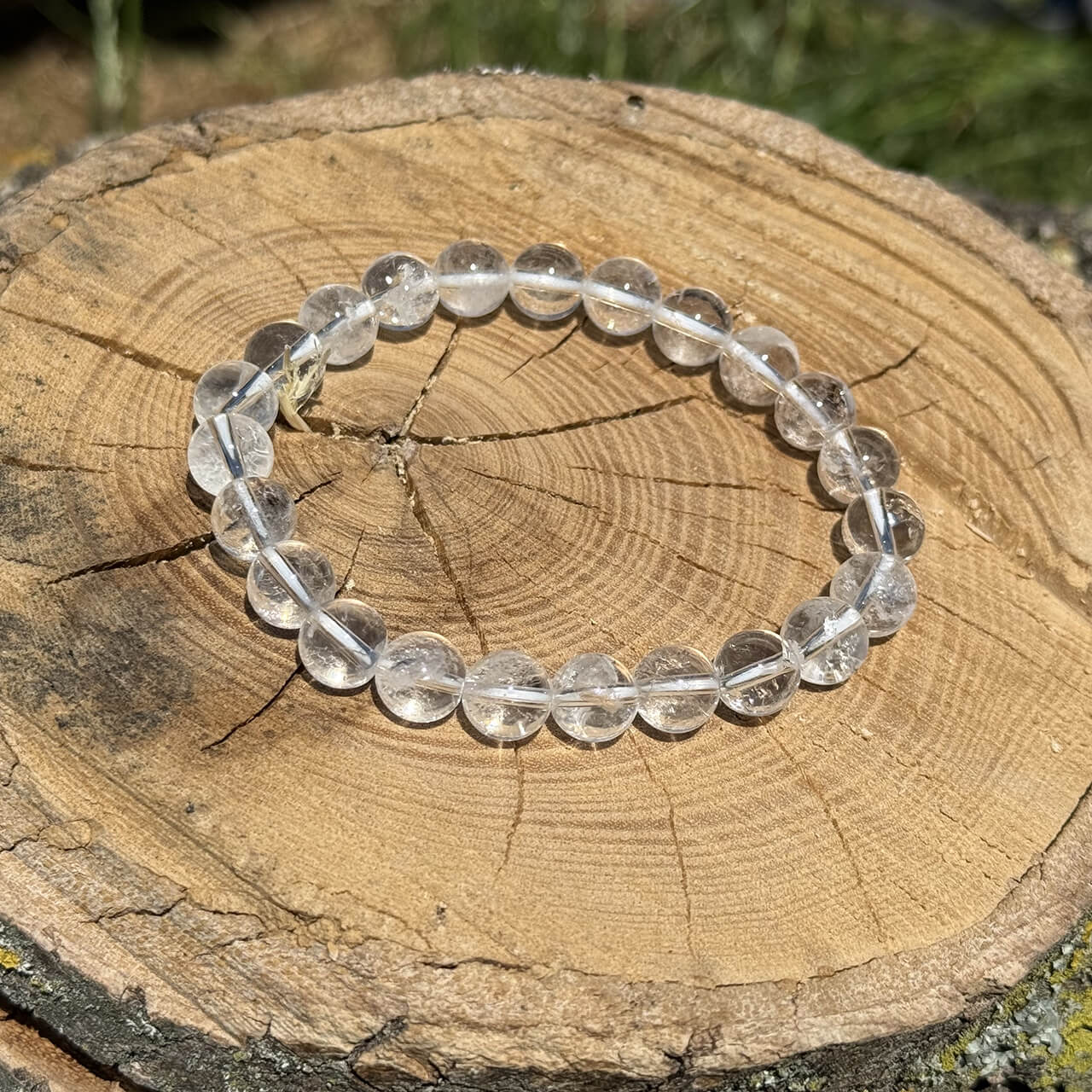 Clear quartz crystal bracelet on wooden block with blurred garden background