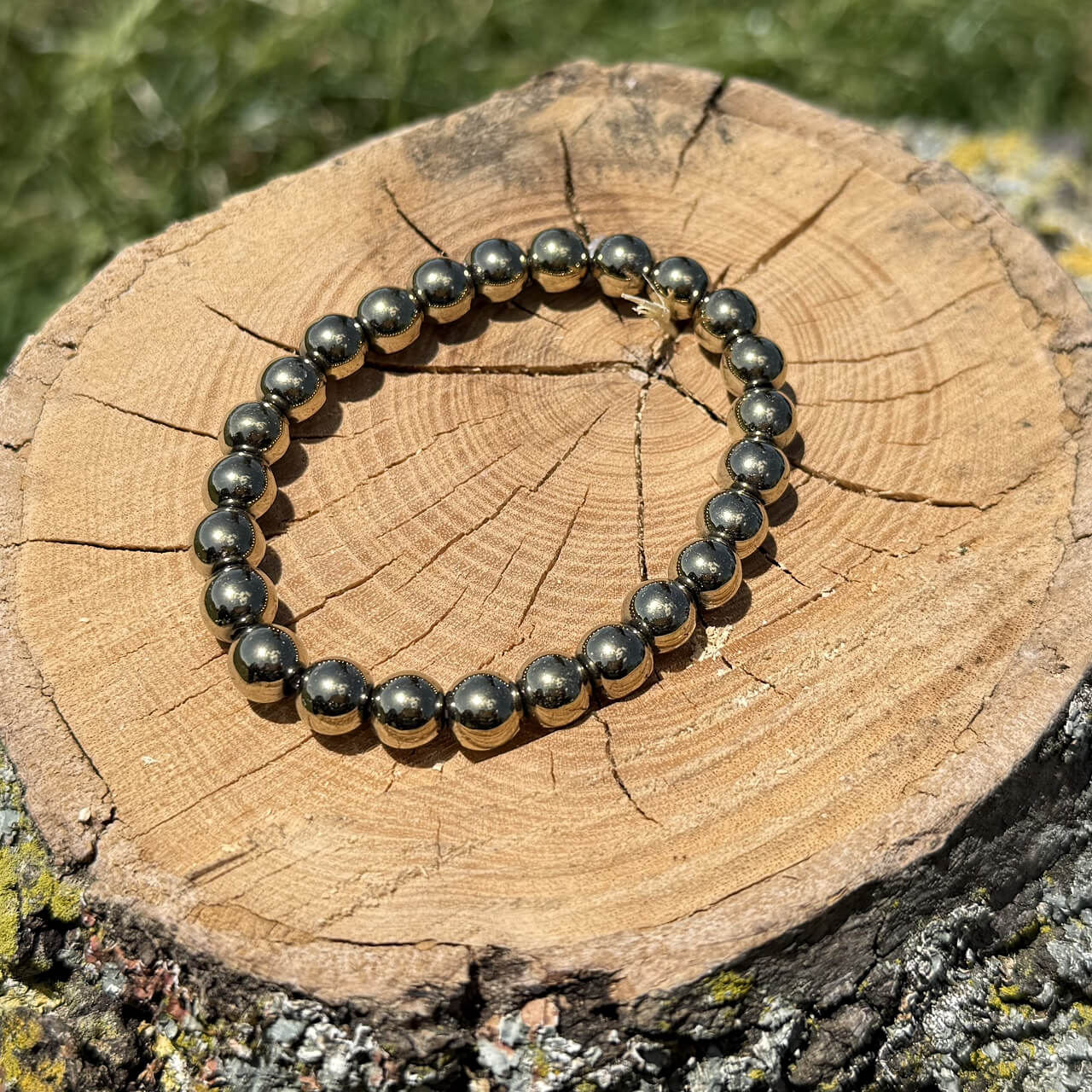 Golden pyrite crystal bracelet on wooden block with blurred garden background