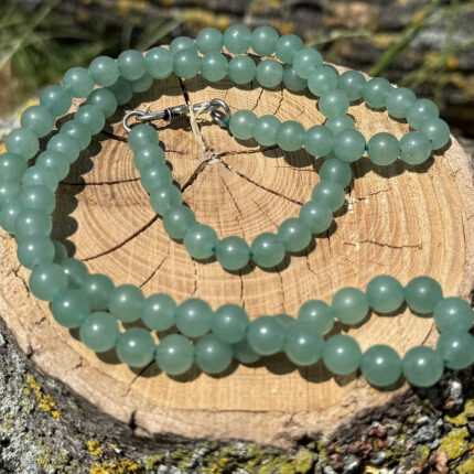 Green aventurine crystal necklace displayed on wooden block with garden grass and greenery background