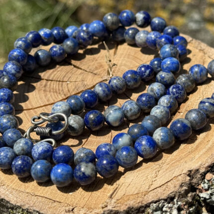 Lapis Lazuli crystal necklace displayed on wooden block with garden grass and greenery background