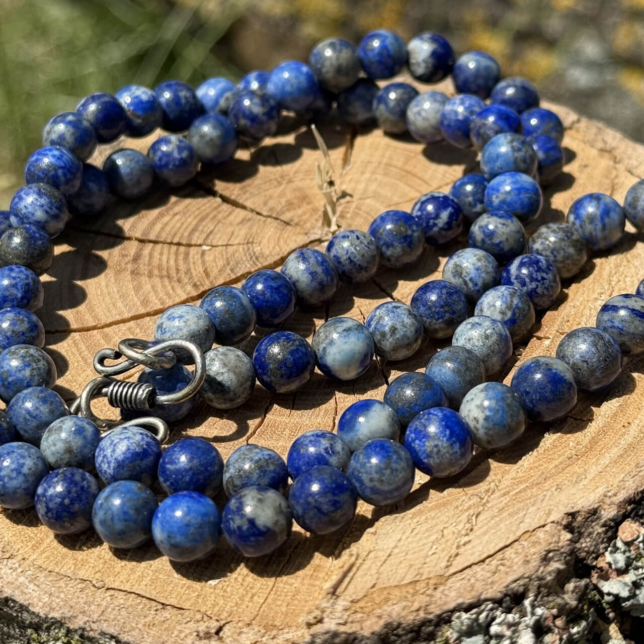 Lapis Lazuli crystal necklace displayed on wooden block with garden grass and greenery background
