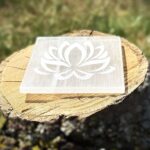 Side view of lotus-engraved Selenite charging plate on wooden block