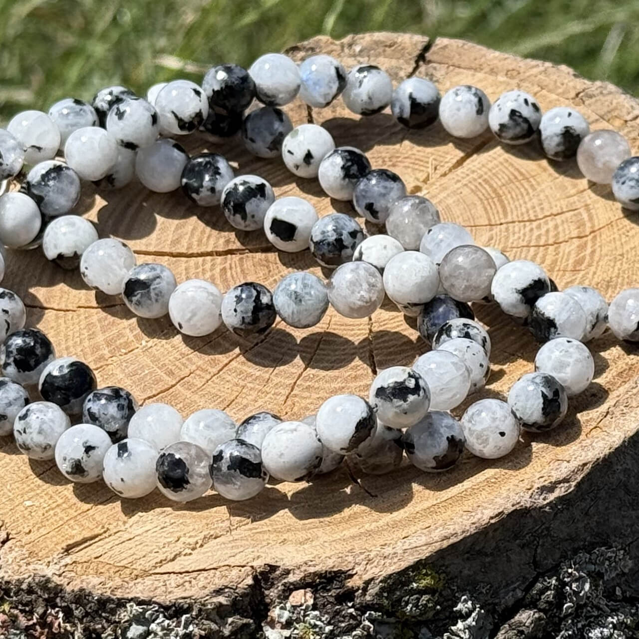Moonstone crystal necklace displayed on wooden block with garden grass and plant background