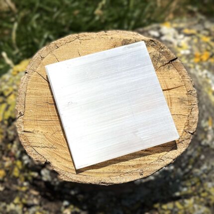Front angled view of 3x3 inch plain Selenite charging plate on wooden block glowing softly