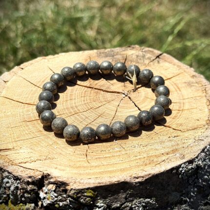 Raw pyrite crystal bracelet with metallic golden-grey beads displayed on wooden log in natural sunlight