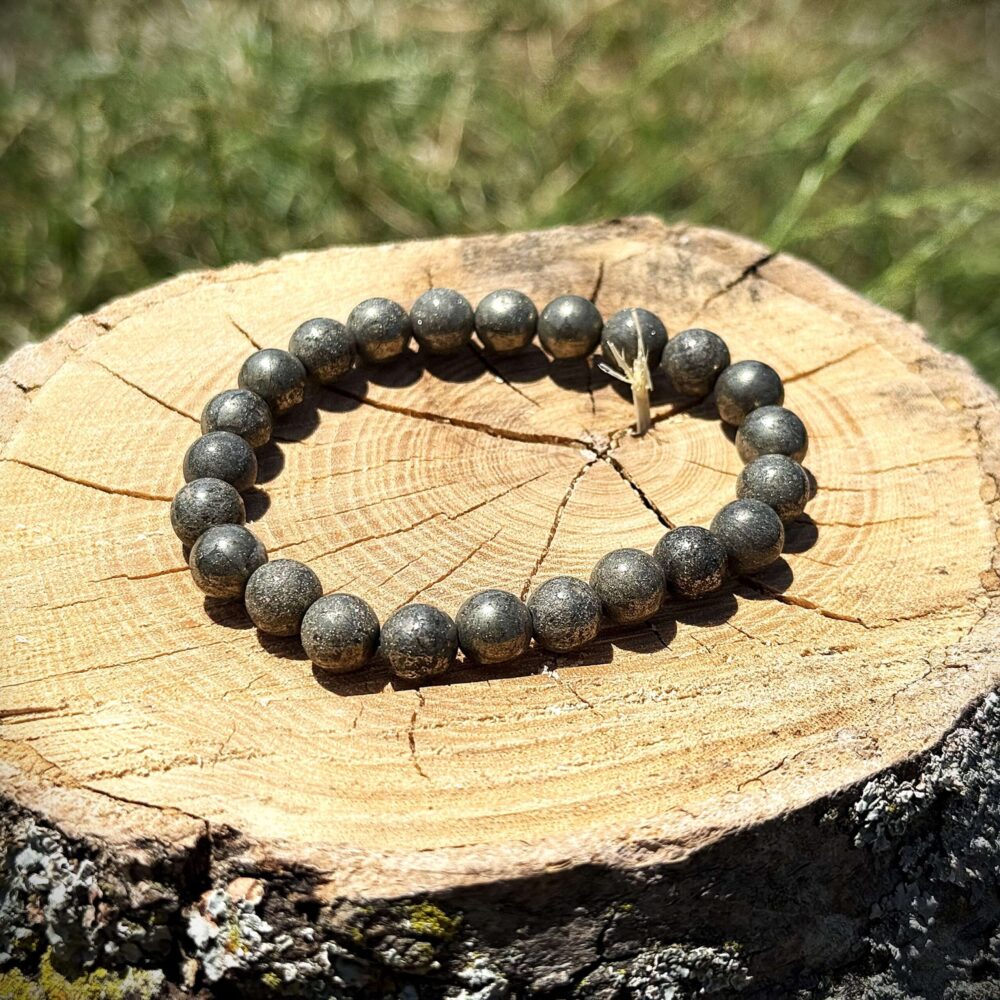 Raw pyrite crystal bracelet with metallic golden-grey beads displayed on wooden log in natural sunlight