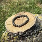 Real natural pyrite crystal bracelet with metallic golden-grey beads displayed on wooden log in natural sunlight
