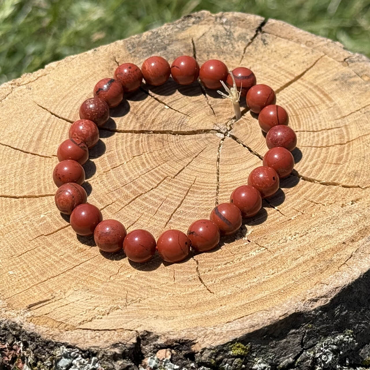 Red jasper crystal bracelet on wooden block with blurred garden background