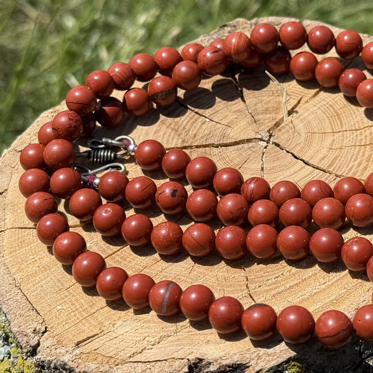 Red jasper crystal necklace displayed on wooden block with garden grass and foliage background
