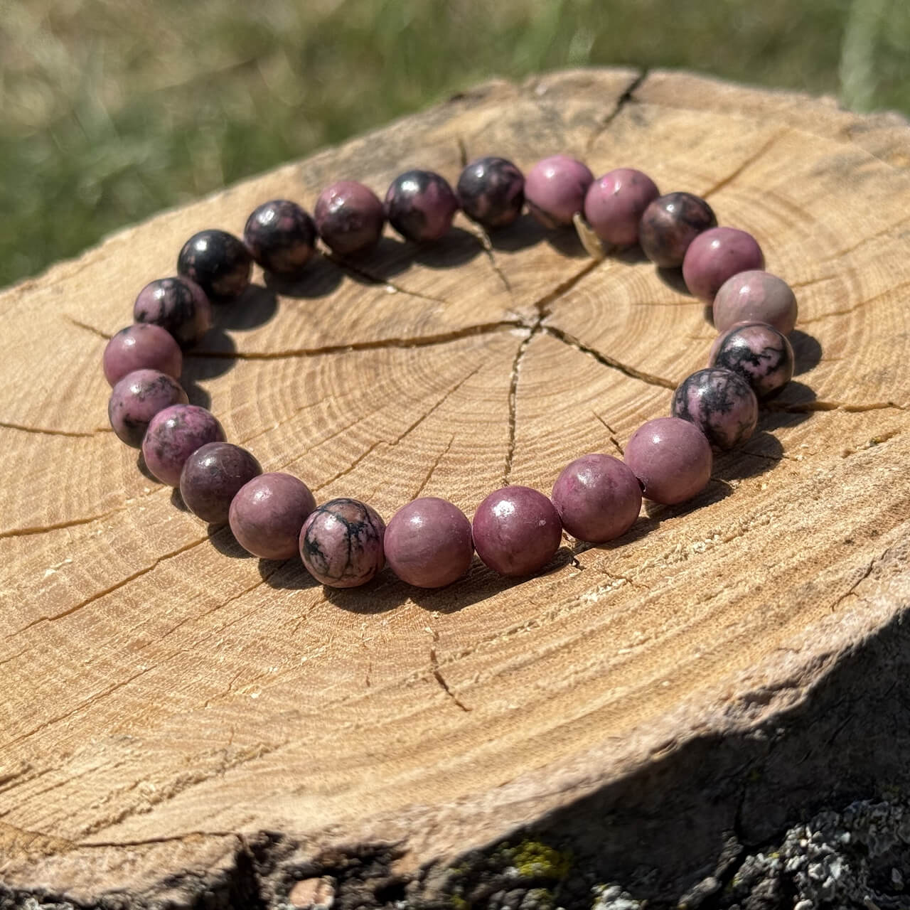 Rhodonite crystal bracelet on wooden block with blurred garden background
