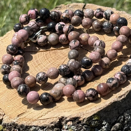 Rhodonite crystal necklace displayed on wooden block with garden grass and greenery background