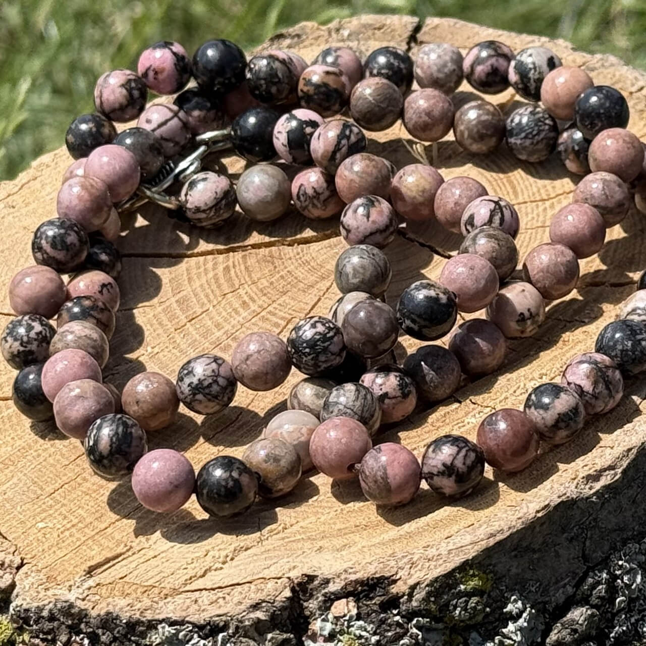 Rhodonite crystal necklace displayed on wooden block with garden grass and greenery background
