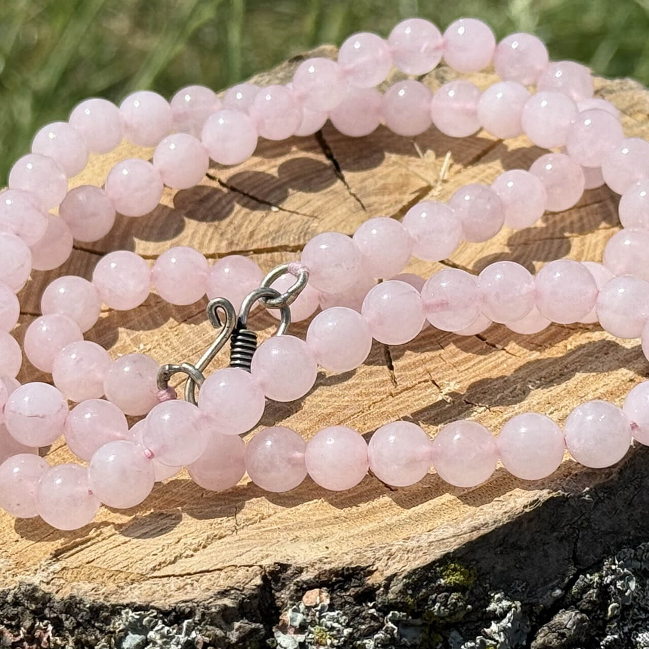 Rose Quartz Necklace displayed on wooden block with garden grass and greenery background